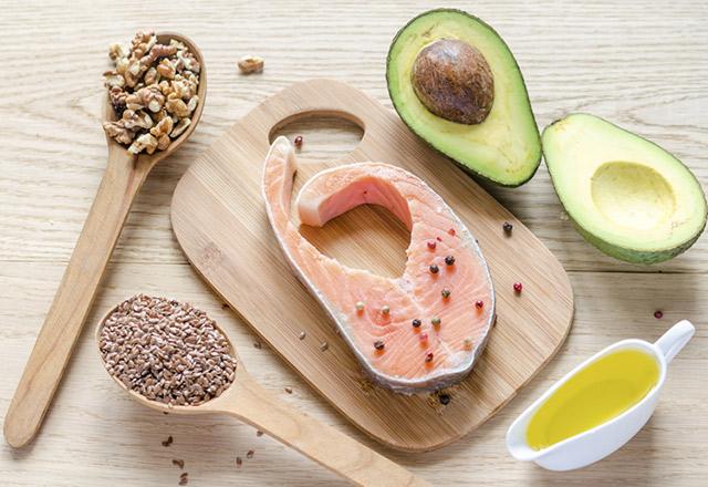 Fish, avocado, nuts and olive oil arranged on a wooden cutting board